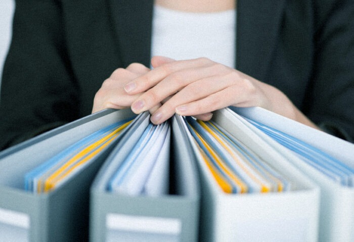 Female hands resting on top of binder folders, with pages and files contained within.