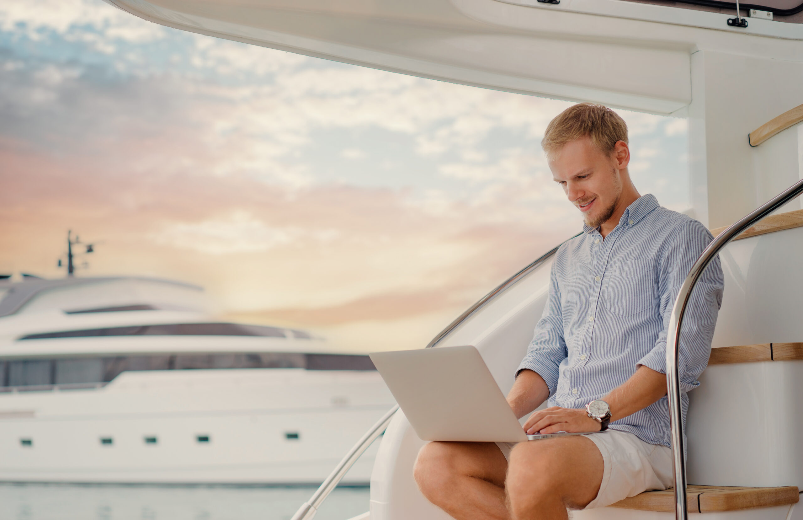 superyacht crew member sits on deck with his laptop on his lap