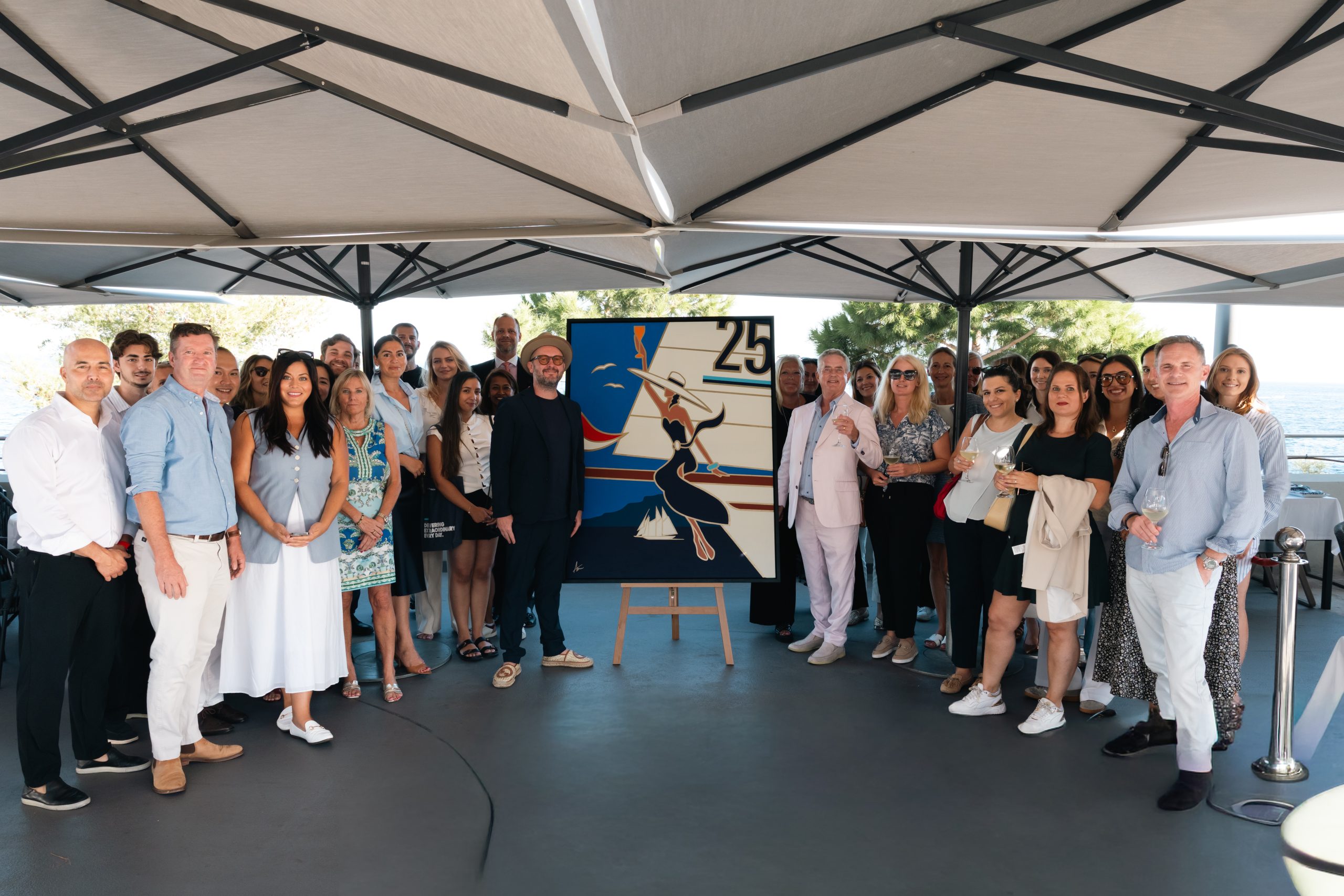 Artist Alan Walsh and Hill Robinson Co-Founder & CEO Niall Robinson present a commissioned 25th-anniversary pop art painting on an easel, surrounded by the Hill Robinson team.